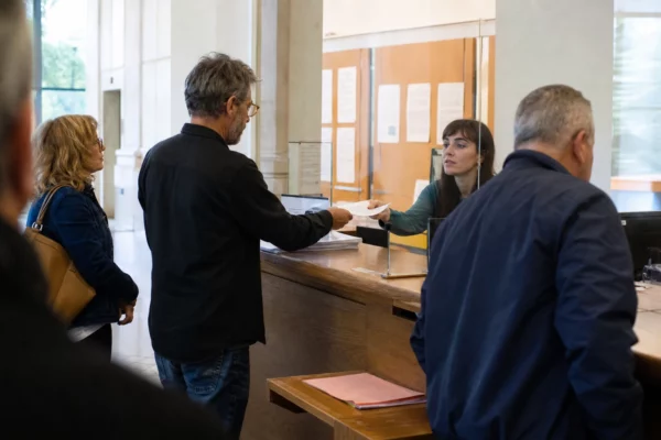 Accueil administratif lumineux avec guichet, dossier papier et usagers anonymes dans une file calme.