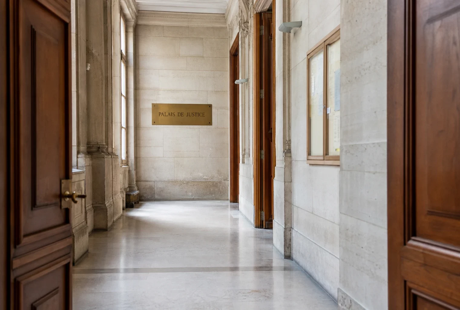 Couloir vide d’un palais de justice français, avec plaque discrète et lumière naturelle claire.