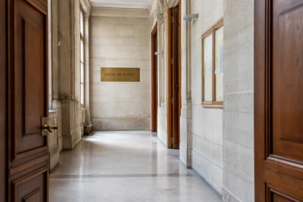 Couloir vide d’un palais de justice français, avec plaque discrète et lumière naturelle claire.