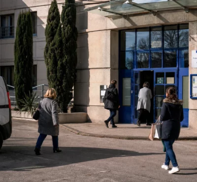 Devant un bâtiment public de protection de l’enfance, des agents anonymes entrent et sortent sous une lumière claire.