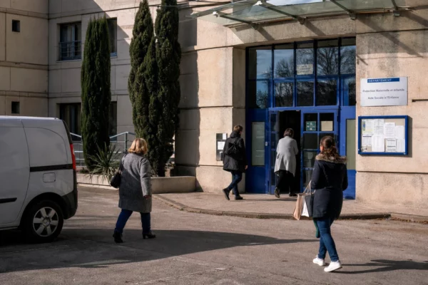 Devant un bâtiment public de protection de l’enfance, des agents anonymes entrent et sortent sous une lumière claire.