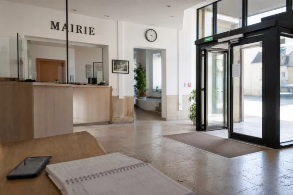 Intérieur lumineux d’une mairie française avec smartphone et agenda flous sur une table, ambiance de service public.