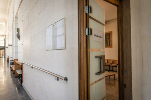 Couloir clair d’un bâtiment institutionnel français, porte d’audition entrouverte et ambiance administrative sobre.