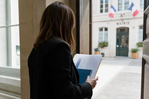 Collaborateur local de dos dans une mairie, dossier en main, dans un couloir lumineux et photographié en contexte réel.