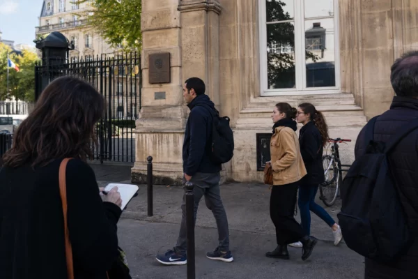 Scène de rue à Paris près d’un bâtiment diplomatique, avec passants anonymes et atmosphère journalistique calme.