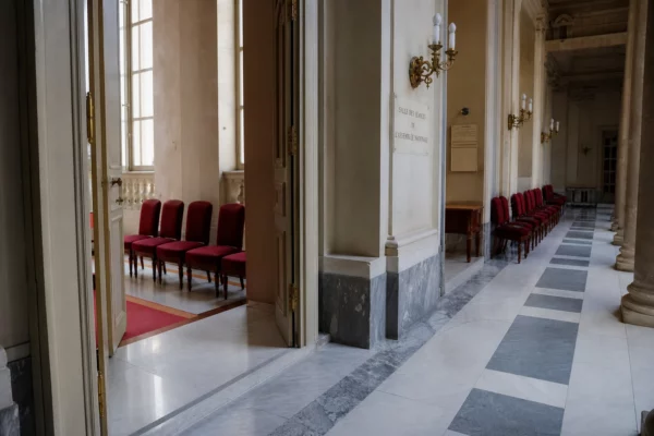 Couloir lumineux de l’Assemblée nationale avec marbre blanc et sièges rouges, dans une ambiance institutionnelle calme.