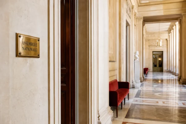 Couloir vide de l’Assemblée nationale à Paris, en lumière naturelle, avec marbre clair et ambiance institutionnelle