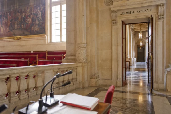 Couloir lumineux de l’Assemblée nationale avec microphones et marbre blanc, vue oblique et atmosphère institutionnelle.