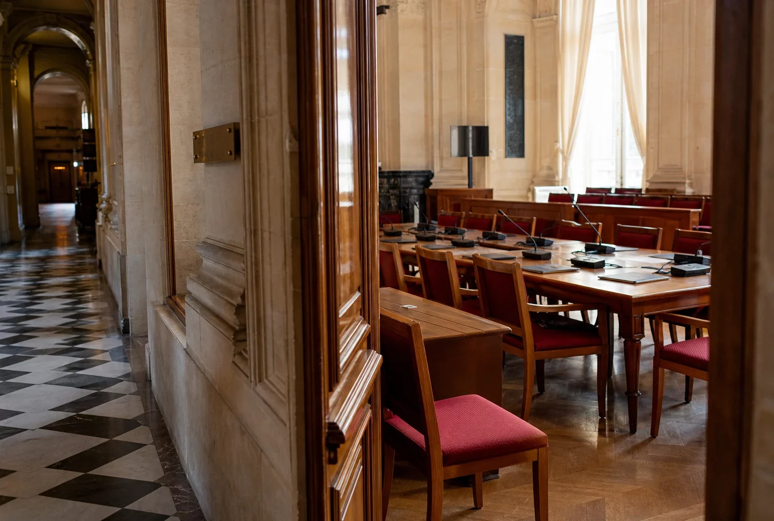 Couloir vide de l’Assemblée nationale avec salle de commission, tables, micros et lumière naturelle claire.