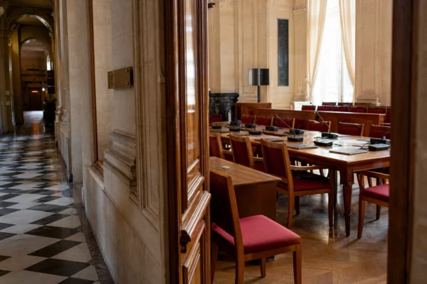 Couloir vide de l’Assemblée nationale avec salle de commission, tables, micros et lumière naturelle claire.