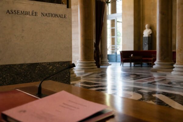 Salle de l’Assemblée nationale en lumière naturelle, avec dossier parlementaire flou et ambiance institutionnelle calme.