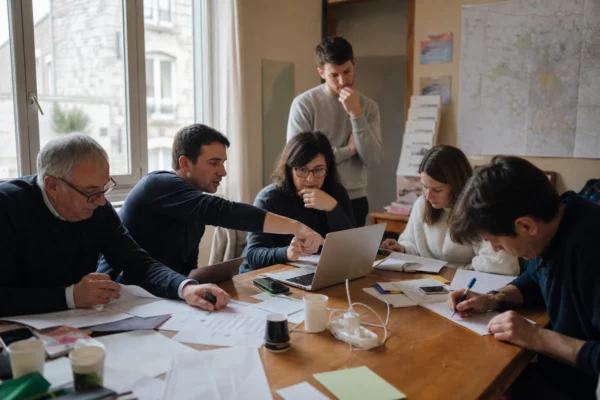 Des militants dans un bureau de campagne local autour d’un ordinateur et de documents, en lumière naturelle.