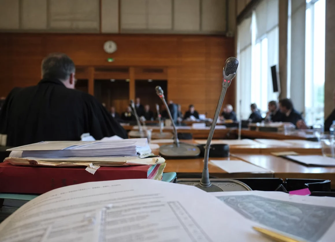 Audition institutionnelle en France avec micros de table, dossiers ouverts et silhouettes anonymes sous une lumière claire.