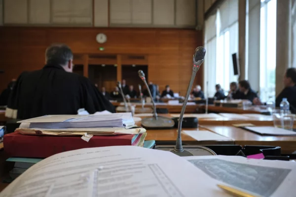 Audition institutionnelle en France avec micros de table, dossiers ouverts et silhouettes anonymes sous une lumière claire.