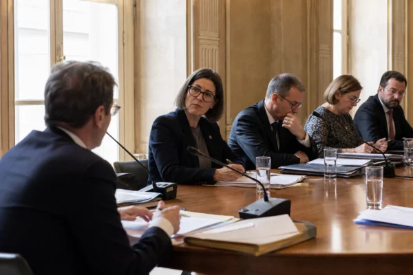 Audition parlementaire en commission au Sénat, avec micros, dossiers ouverts et silhouettes anonymes dans une salle claire.