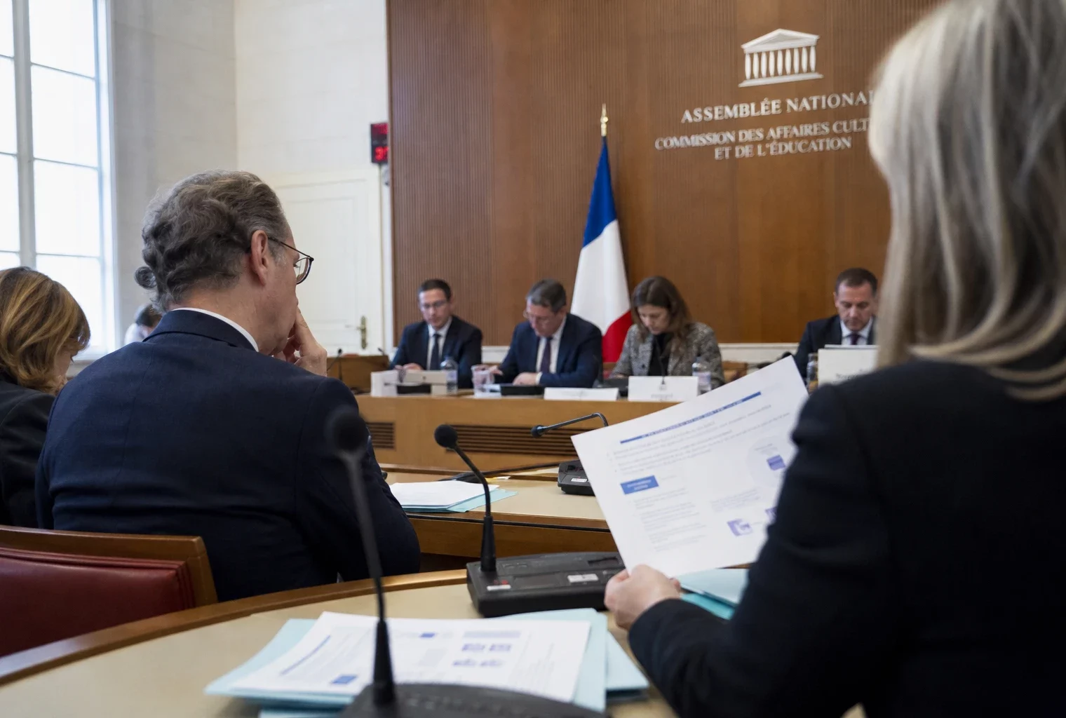 Audition parlementaire sur l’IA et le droit d’auteur, avec micros, dossiers flous et silhouettes anonymes dans une salle claire.