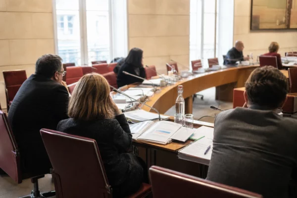Audition parlementaire dans une salle claire du Sénat, avec micros, dossiers ouverts et silhouettes anonymes.