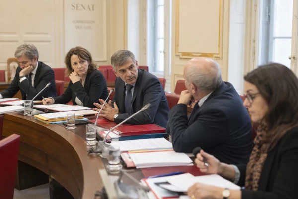 Réunion de commission au Sénat avec plusieurs responsables anonymes, micros, dossiers ouverts et lumière naturelle.