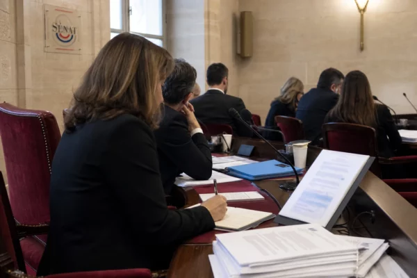 Audition au Sénat sur la régulation du privé, avec micros, dossiers ouverts et silhouettes anonymes en salle claire.