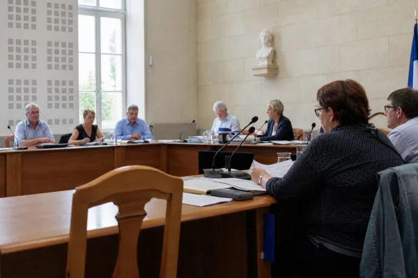 Salle municipale française avec chaise vide, micros et dossiers flous lors d’un débat local sur l’autonomie corse