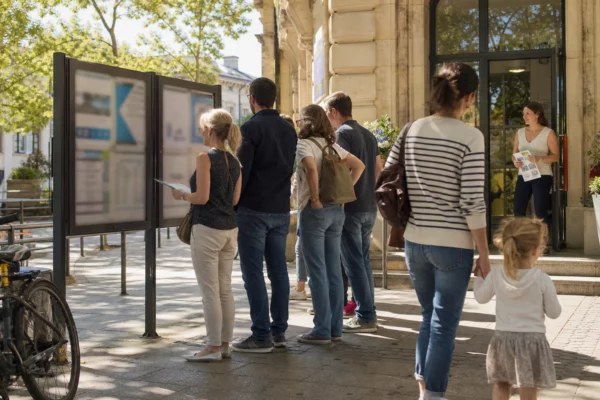 Des habitants devant une mairie de banlieue consultent un panneau municipal sur la baignade dans la Seine.
