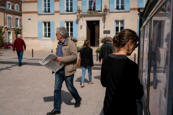 Des passants anonymes devant une mairie française en centre-ville, dans une ambiance de vie citoyenne et politique discrète.