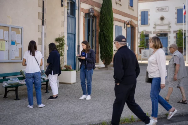 Place de mairie en province avec habitants anonymes, reporter local et fleurs discrètes dans une ambiance calme et lumineuse.