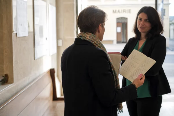 Un élu local anonyme échange dans un couloir de mairie avec un carnet et un dossier à la main.