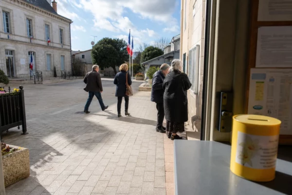 Place d’une petite ville française avec mairie, habitants anonymes et ambiance documentaire autour d’une action caritative.