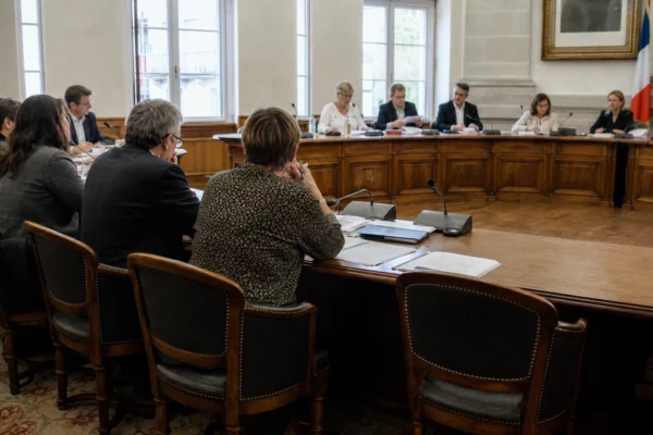Salle municipale française lumineuse avec micros, dossiers et chaise vide lors d’une réunion locale