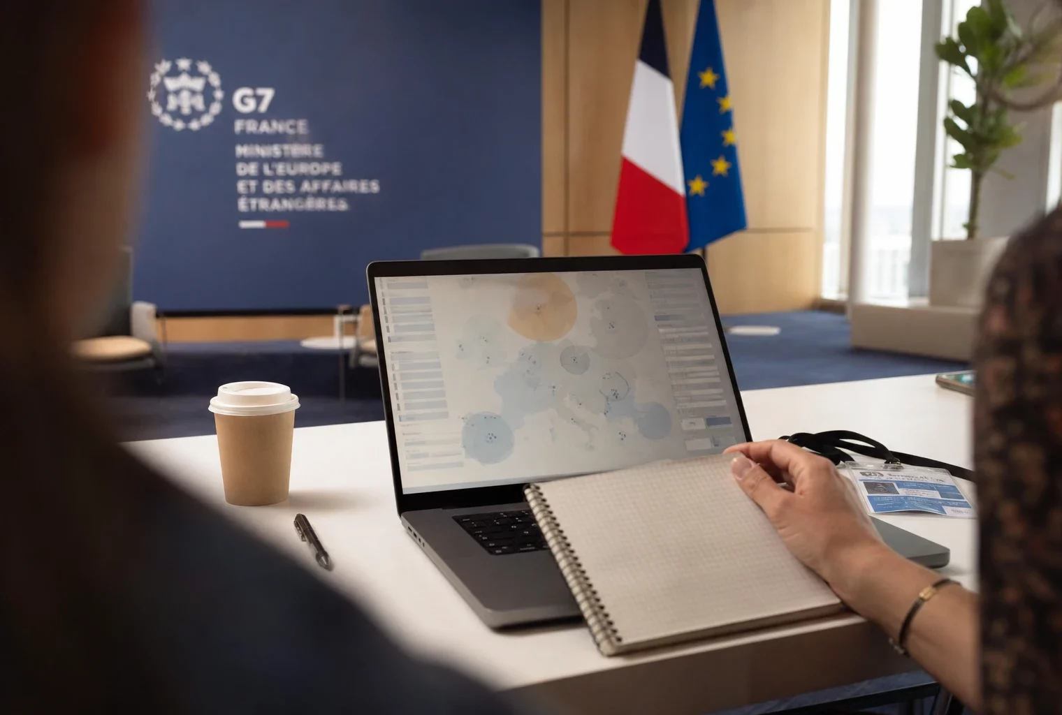 Vue de dos sur un bureau de briefing avec un écran affichant une interface européenne abstraite, en lumière naturelle claire.