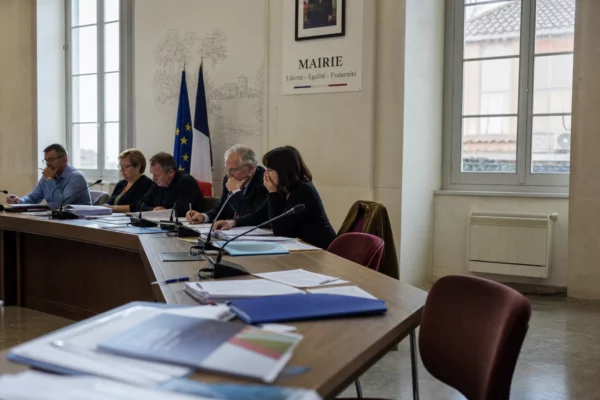 Salle municipale française avec chaises vides, micros et dossiers flous pour illustrer le budget européen.