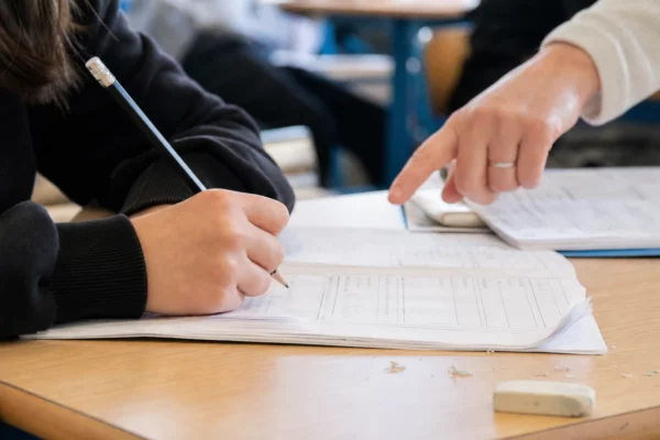 Gros plan d’une main d’élève annotant un cahier sur un bureau de classe lumineux