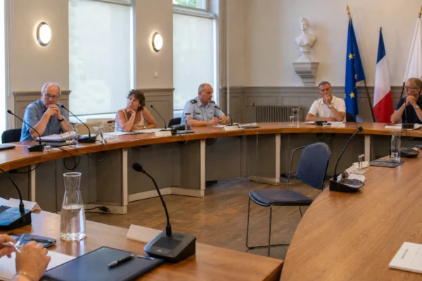 Salle municipale française avec micros, dossiers et chaise vide lors d’un débat sur la chaleur au travail