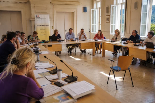 Salle municipale en plan large avec chaise vide, micros et dossiers flous lors d’une réunion sur la canicule.