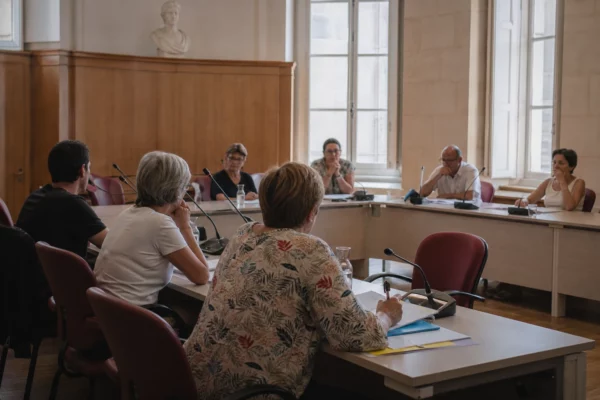 Salle municipale lumineuse avec micros, dossiers et chaise vide lors d’une réunion sur la canicule