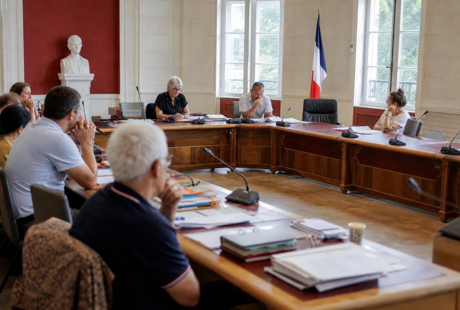 Salle municipale lumineuse avec chaise vide, micros et dossiers pour un débat sur l’adaptation à la canicule.