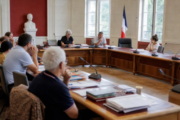 Salle municipale lumineuse avec chaise vide, micros et dossiers pour un débat sur l’adaptation à la canicule.