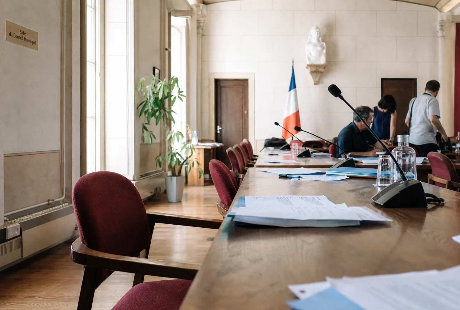 Salle municipale lumineuse avec chaises vides, micros et dossiers pour une réunion sur la canicule.