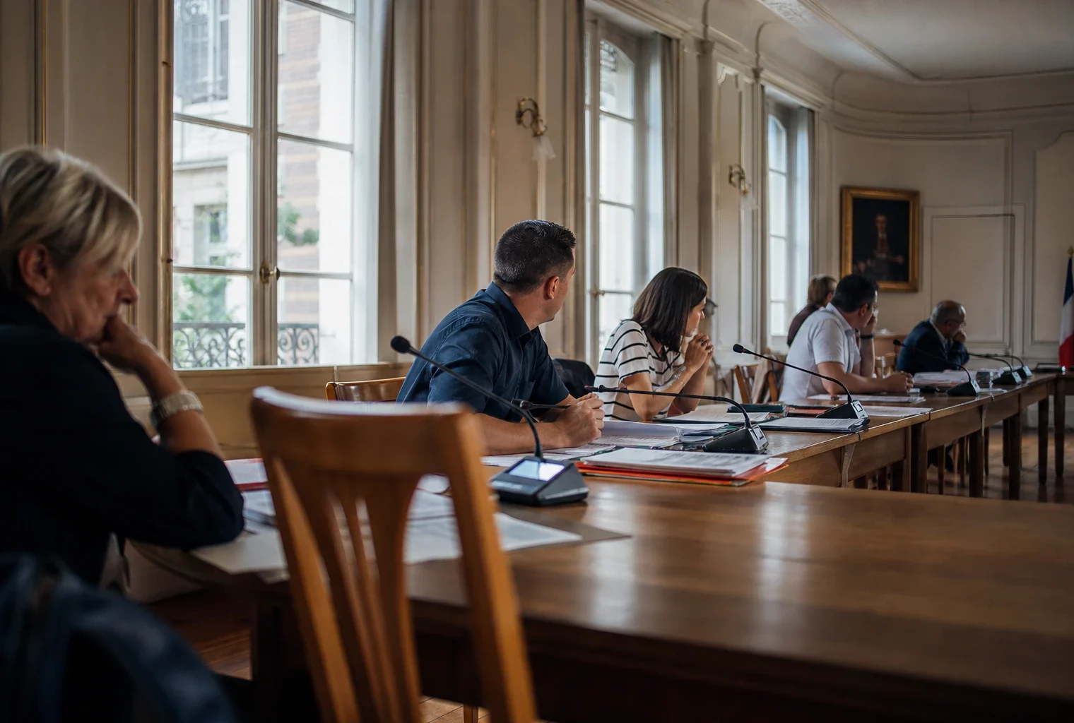 Salle municipale avec micros, dossiers et chaise vide pendant un conseil local sur la canicule
