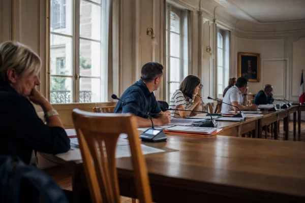 Salle municipale avec micros, dossiers et chaise vide pendant un conseil local sur la canicule