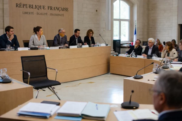 Salle municipale de conseil local avec une chaise vide, des micros et des dossiers flous, sous lumière naturelle.