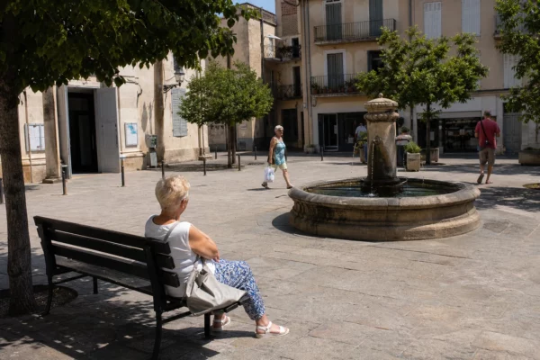 Place d’une ville moyenne française sous une forte chaleur, avec habitants anonymes, ombres nettes et ambiance de reportage.
