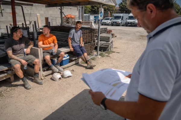 Ouvriers sur un chantier français en pause sous la chaleur, avec eau, ombre et matériel de travail.