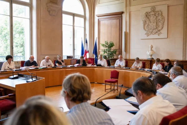 Salle du conseil municipal de Castres avec micros, dossiers et une chaise vide dans une ambiance de séance municipale