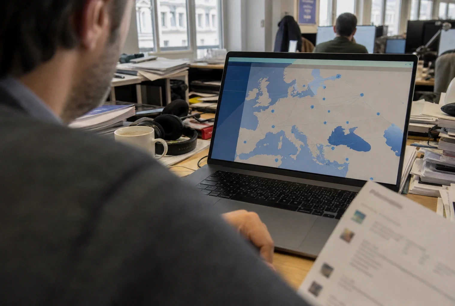 Dans une rédaction parisienne, un journaliste consulte un écran avec une carte européenne abstraite sur le Liban.