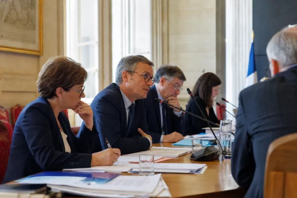 Réunion de commission parlementaire en France avec micros, dossiers ouverts et élus anonymes autour d’une table.