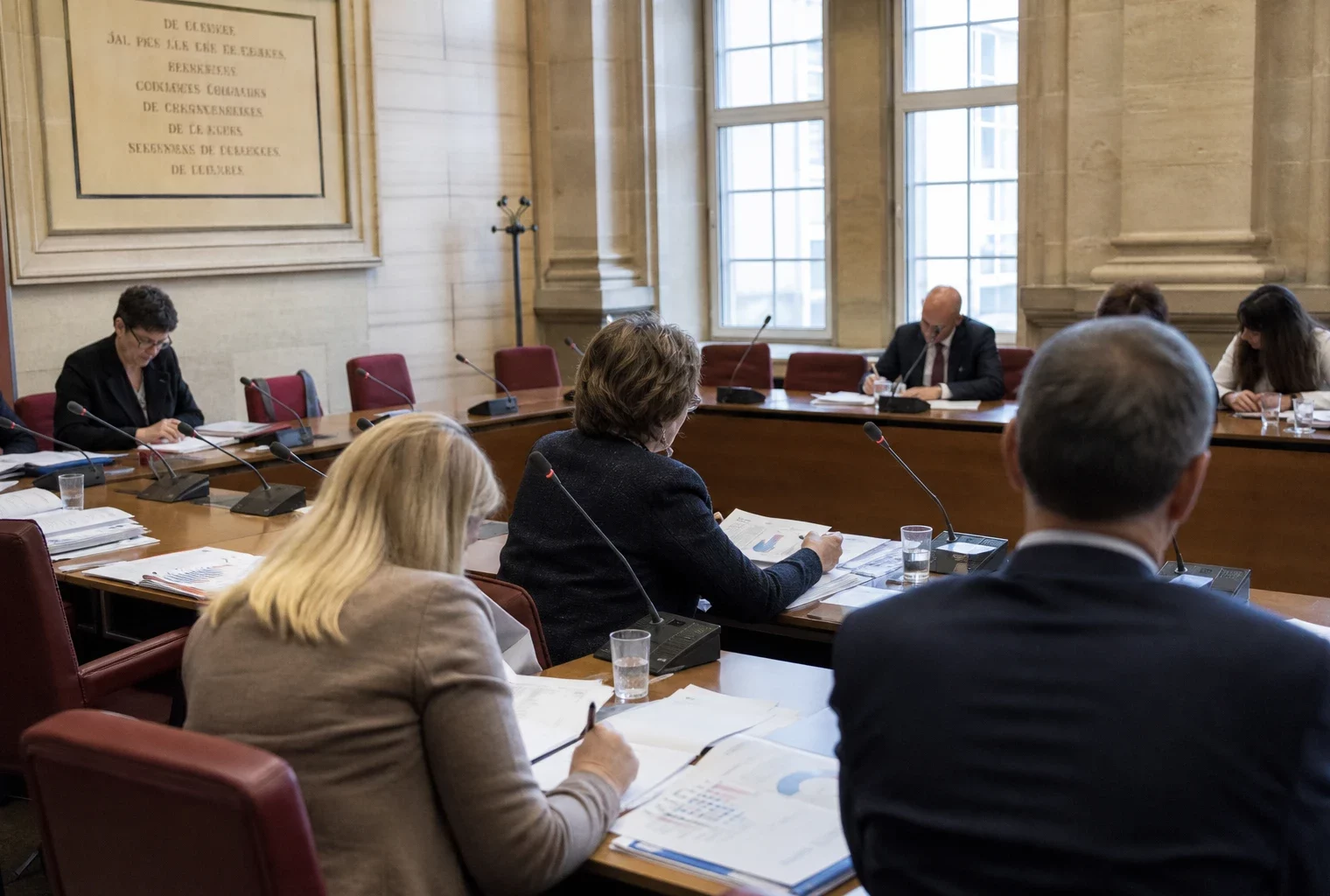 Réunion de commission au Parlement européen avec micros, dossiers et silhouettes anonymes autour d’une table