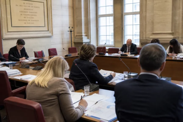 Réunion de commission au Parlement européen avec micros, dossiers et silhouettes anonymes autour d’une table