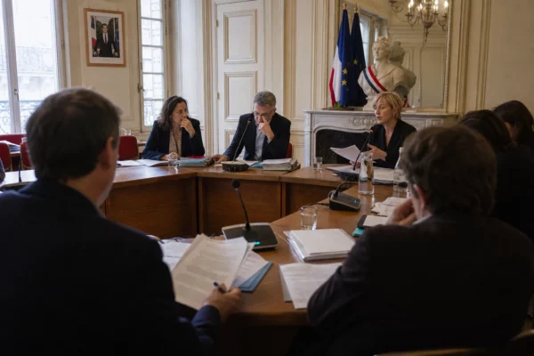 Réunion de commission municipale en France avec élus anonymes, micros, dossiers et lumière naturelle claire.